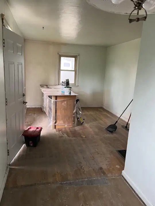 Room stripped back to the old floor during a renovation, broom and debris tote by the wall