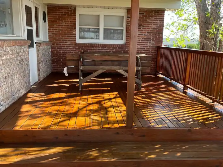 Covered deck on a brick home, boards and cedar railing freshly stained in late sun