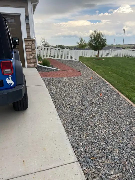 Gravel walkway running beside a concrete driveway to a white fence