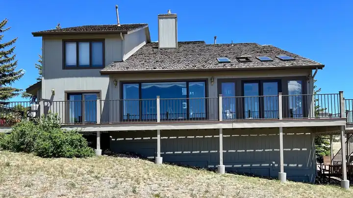 Two-storey home with a long rear deck under a clear blue sky after repainting